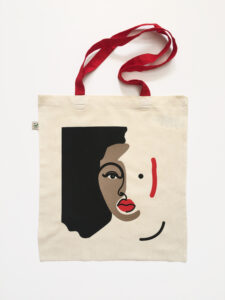 A natural tote bag with a contrast red strap and 3 colour screen print of an abstract face.