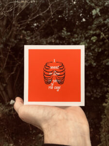 A screen printed greeting card with the text 'I want to live in your rib cage' encompassed by an illustration of a rib cage.